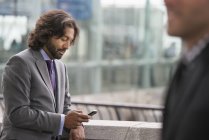Two men in business suits on terrace with railing checking phone. — Stock Photo