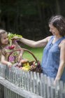 Mother and daughter standing in garden with basket of vegetables. — Stock Photo