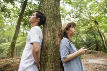 Couple japonais appuyé sur le tronc d'arbre dans la forêt, femme tenant tablette numérique
. — Photo de stock