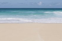 Agua turquesa vívida y olas rompiendo en la playa de arena . - foto de stock