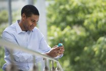 Мужчина, опирающийся на перила в парке и проверяющий смартфон . — стоковое фото