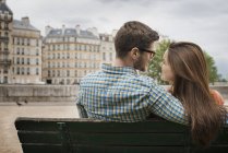 Mid adult couple sitting close together on bench by River Seine in Paris, France. — Stock Photo