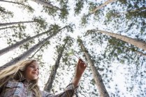 Low angle view of pre-adolescent girl in woods with tall trees background. — Stock Photo