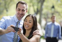 Пара бере селфі зі смартфоном з чоловіком, що стоїть на задньому плані . — стокове фото
