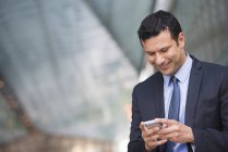 Mid adult businessman in business suit smiling and using phone. — Stock Photo