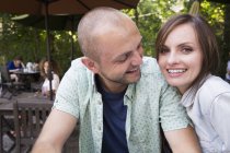 Couple sitting together in outdoor cafe and looking in camera. — Stock Photo