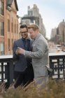 Two businessmen standing side by side and looking at mobile phone in city. — Stock Photo