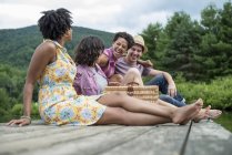 Small group of people sitting on wooden pier overlooking country lake. — Stock Photo
