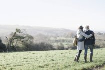 Dos mujeres de pie lado a lado y abrazándose en la pendiente de hierba con vistas al paisaje de Dorset, Inglaterra . - foto de stock