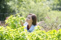 Junge Frau umgeben von grünen Pflanzen, die draußen sitzen. — Stockfoto