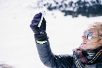 Mulher segurando smartphone no braço estendido no inverno . — Fotografia de Stock