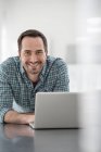 Man leaning on office table with laptop and looking in camera. — Stock Photo