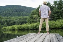 Vista trasera del hombre de pie en el muelle de madera con vistas al lago tranquilo . - foto de stock