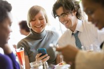 Man and woman sharing smartphone at restaurant table with friends. — Stock Photo
