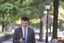 Jovem empresário em terno cinza e gravata usando smartphone . — Fotografia de Stock