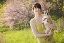 Mujer joven en campo herboso en primavera sosteniendo perro chihuahua . - foto de stock