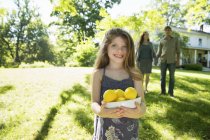 Chica sosteniendo cajón de limones con adultos en el fondo . - foto de stock