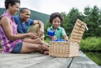 Familie mit Grundschulkind sitzt auf Seebrücke mit Picknickkorb. — Stockfoto