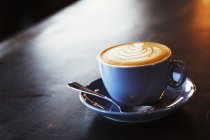 Coupe de cappuccino mousseux dans une tasse avec soucoupe sur une table en bois
. — Photo de stock