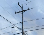 Telefonmast und Stromleitungen gegen bewölkten Himmel, Blick in den niedrigen Winkel. — Stockfoto