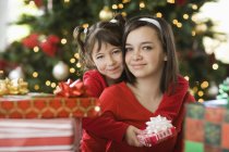 Two girls side by side by Christmas tree surrounded by presents. — Stock Photo