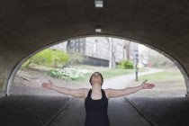 Mujer en Central Park haciendo yoga bajo puente con los brazos extendidos . - foto de stock