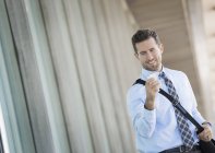 Young man with shoulder bag using smartphone outside office building. — Stock Photo