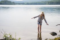 Teen girl in straw hat balancing in shallow water of country lake. — Stock Photo
