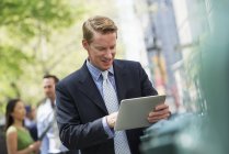 Mittlerer erwachsener Mann mit digitalem Tablet auf der Stadtstraße mit Paar im Hintergrund. — Stockfoto