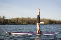Woman doing headstand on paddle board on lake. — Stock Photo