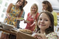 Elementary age girl looking in camera at table with adults in background. — Stock Photo