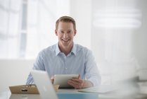 Бизнесмен улыбается и держит цифровой планшет в воздушной офисной среде . — стоковое фото