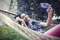 Frau liegt in Gartenhängematte und macht Selfie mit Handy. — Stockfoto