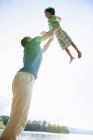 Низький кут зору батька, що грає і піднімає хлопчика початкового віку на відкритому повітрі . — стокове фото