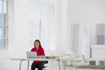 Средне взрослая азиатка сидит за столом и пользуется ноутбуком в офисе . — стоковое фото