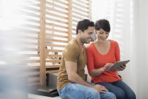 Couple sitting by window at home and using digital tablet. — Stock Photo