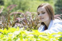 Молода жінка в саду вивчає зростаючі рослини . — стокове фото