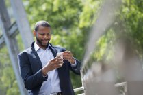 Businessman in blue jacket using smartphone on city street. — Stock Photo