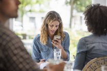 Woman checking smartphone while sitting with friend in coffee shop interior. — Stock Photo