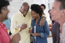 Man and woman smiling and embracing with glasses and people at party. — Stock Photo