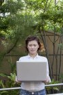 Front view of woman holding laptop and looking down while standing outdoors. — Stock Photo