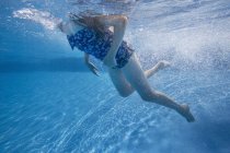 Pre-adolescent girl swimming underwater in pool. — Stock Photo