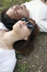 Overhead view of young Japanese man and woman in sunglasses lying on ground. — Stock Photo