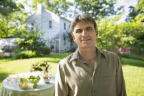 Man in farmhouse garden standing beside round table with fresh vegetables and fruits. — Stock Photo