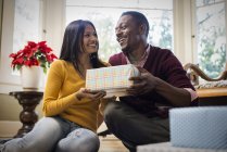 Low angle view of couple by sofa exchanging wrapped presents. — Stock Photo