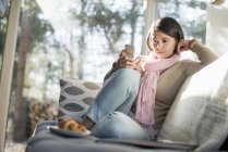 Woman sitting on sofa and using smartphone with plate with croissant in front. — Stock Photo