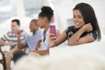 Woman using pink smartphone with people talking at party in background. — Stock Photo