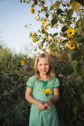 Pre-adolescent girl standing in garden and holding sunflower. — Stock Photo