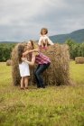 Mother playing outdoors with daughters and lifting girl on haystack. — Stock Photo