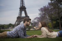 Paar auf Gras liegend und Händchen haltend im Schatten des Eiffelturms in Paris, Frankreich. — Stockfoto